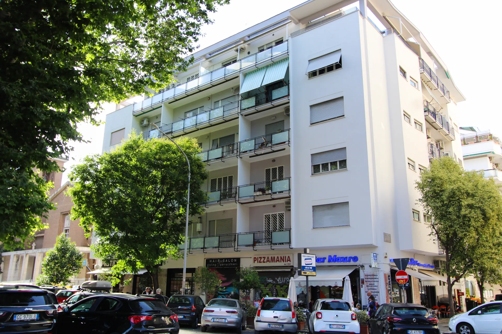 Palazzo YOU Rhome in Garbatella, Via Manfredo Camperio 9 — facciata su via con bar e negozi di quartiere